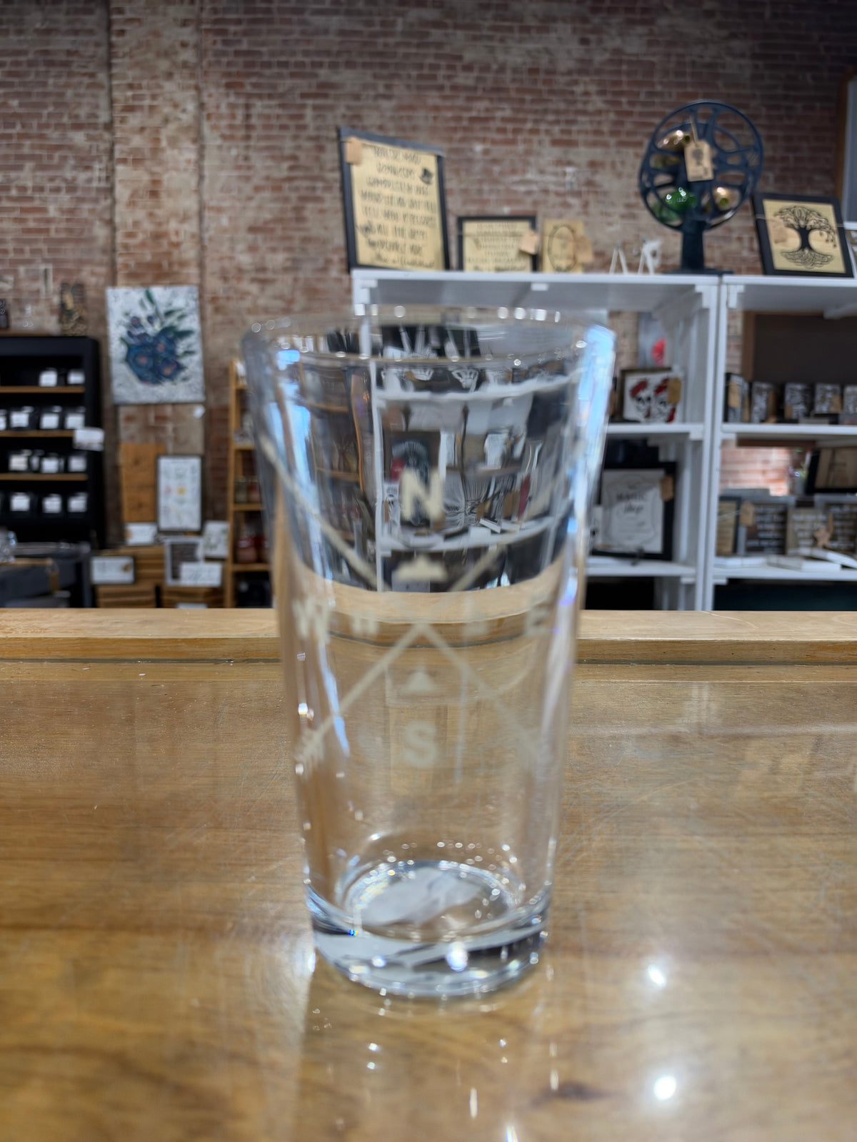 Empty clear Arrow Compass pint glass on a wooden counter