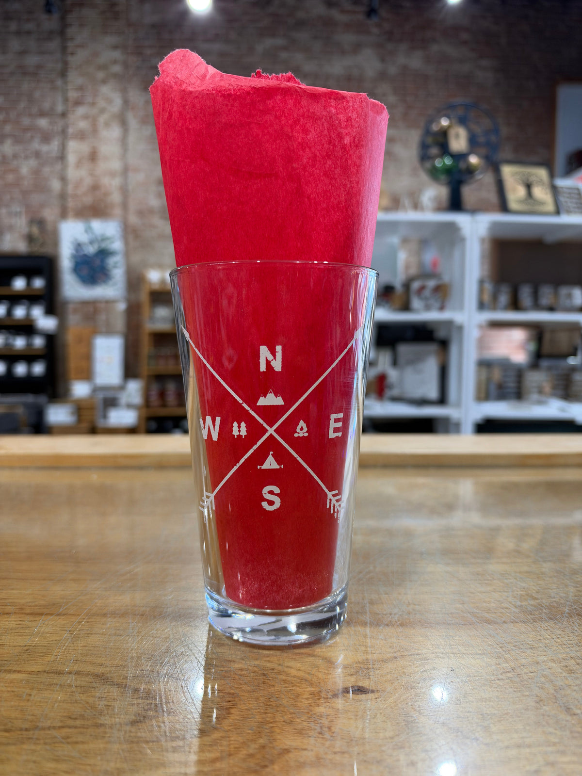 Arrow Compass pint glass showing white compass directions and outdoor symbols against red tissue paper